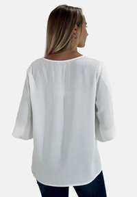 Witte, losvallende blouse met driekwartmouwen, gemaakt van een lichtgewicht stof. Zachte textuur en ronde halslijn aan de achterkant.