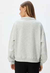 Ljust grå sweatshirt med rundad nacke och ribbade ärmslut. Har neddragen axel och en avslappnad passform, tillverkad av mjukt, texturerat tyg.