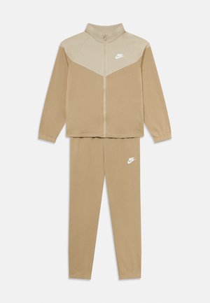 Ensemble de sport Nike beige en deux pièces, composé d'une veste zippée avec un empiècement plus clair et d'un pantalon assorti, tous deux ornés de logos Nike blancs.