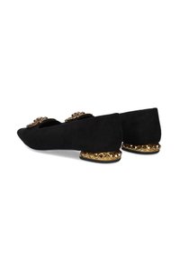 Zapatos planos de ante negro con punta afilada, embellecidos con herrajes dorados y un lazo decorativo, con un acento dorado con tachuelas en el tacón.