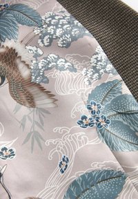 Textil med pastellrosa siden och blommönster samt vågmönster i blått och vitt, kompletterat med en mörk hounds-tooth kant.