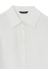 Chemise blanche à col avec petits boutons sur le devant et une étiquette noire indiquant le nom de la marque Calliope et la taille S.