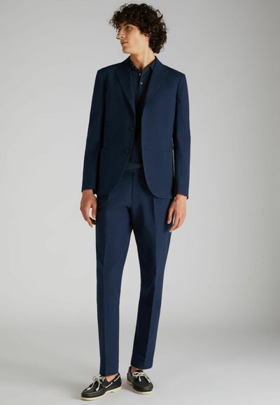 Granatowy, strukturalny garnitur z dopasowaną marynarką i slim-fit spodniami. Połączony z czarnymi butami z białymi sznurowadłami i okrągłym noskiem.