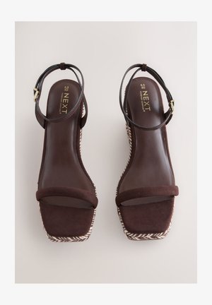 Brune kilehæls-sandaler med øvre del i ruskind, ankelrem med metalspænde og en tekstureret vævet platform. Glat indersål med minimal detaljering.