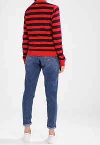 Suéter a rayas rojas y marinas con un cuello acanalado, combinado con pantalones vaqueros azul rectos y zapatillas blancas. Conjunto casual con costuras visibles.