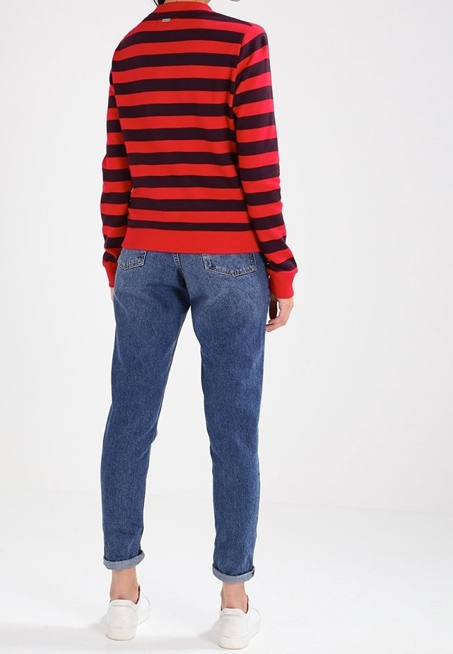 Suéter a rayas rojas y marinas con un cuello acanalado, combinado con pantalones vaqueros azul rectos y zapatillas blancas. Conjunto casual con costuras visibles.