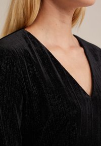 Black velvet top with a deep V-neckline, featuring a subtle textured pattern and sheen. Visible shoulder seam and clean edges.