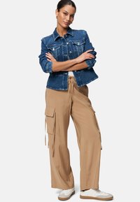 Denim jacket met knoopsluiting, lichtblauwe kleur, medium gewicht. Beige cargobroek met zijzakken en een losse pasvorm. Witte sneakers.