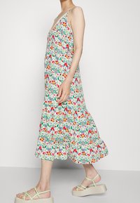 Abito floreale con scollo a V, spalline regolabili e orlo a strati. I colori includono rosso, rosa, blu e verde su uno sfondo bianco.