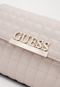 Lyserød quiltet clutch med en glat tekstur, der har et gyldent "GUESS" logo og en rektangulær metalaccent.