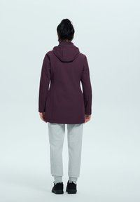 Giacca leggera bordeaux con cappuccio, maniche lunghe e design aderente, abbinata a pantaloni della tuta grigi e scarpe nere.