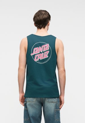 Vyras dėvi žalsvą be rankovių marškinėlį su rožiniu „Santa Cruz Skateboards“ logotipu nugaroje, derinį sudaro mėlyni džinsiniai kargo šortai.