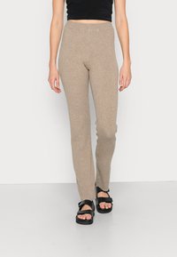 Leggings bege canelados com uma cintura alta, design ajustado e uma textura suave, combinados com sandálias pretas de tiras.