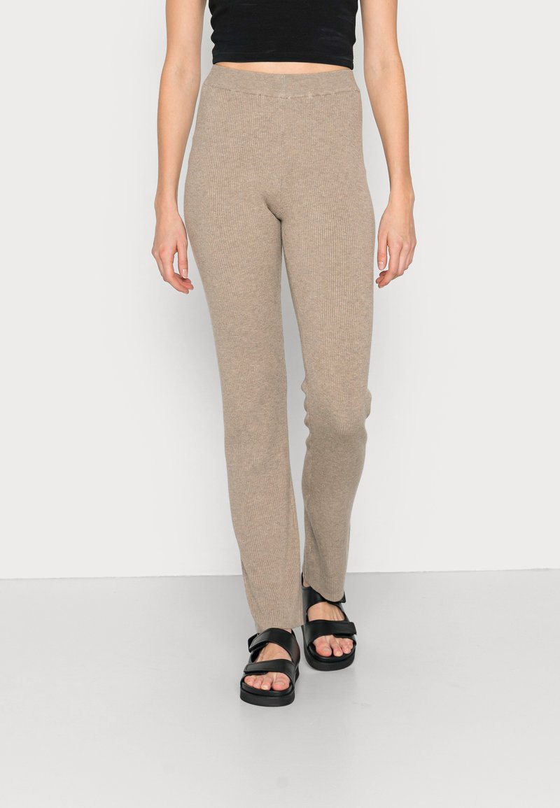 Leggings bege canelados com uma cintura alta, design ajustado e uma textura suave, combinados com sandálias pretas de tiras.