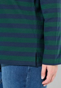 Groen en marineblauw gestreept overhemd met lange mouwen, voorzien van een zijsplit en gemaakt van zachte katoen, gecombineerd met blauwe denim jeans.