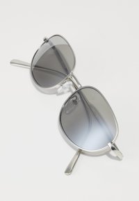 Lunettes de soleil avec une monture en métal argenté, des verres teintés gris et une forme rectangulaire. Elles comprennent des plaquettes de nez et des branches fines.