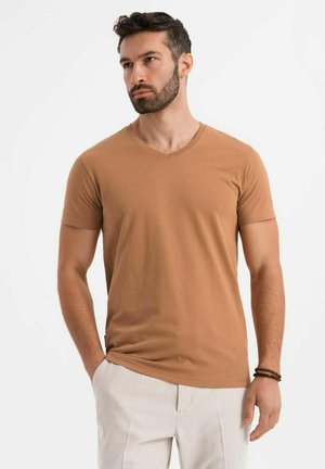 Camiseta marrón de cuello en V y manga corta, hecha de algodón, con un corte ajustado y una textura suave, combinada con pantalones de colores claros.