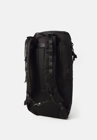Zaino nero con spallacci imbottiti, schienale in rete testurizzata, scomparti con zip multipli e tasche laterali per accessori. Costruzione in tessuto resistente.