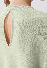 Gestrickter Pullover in hellgrün mit rundem Ausschnitt, offenem Schlüsselloch-Detail im Rücken und strukturiertem Stoff. Verfügt über gerippte Kanten am Ausschnitt.