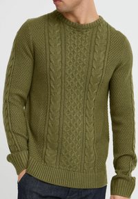 Pulover tricotat de culoare verde măsliniu, cu motive de cabluri și texturi, guler rotund și manșete și tiv din material rib. Fabricat dintr-un material moale.