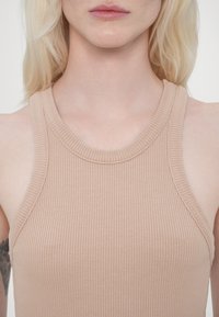 Ráncos, ujjatlan felső puha bézs színben; kerek nyakkivágással és enyhe textúrával rendelkezik. Egyszerű és testhezálló dizájn.