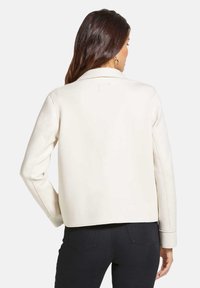 Crème-kleurige neplederen jas met een kraag, lange mouwen en een licht cropped pasvorm. Beschikt over nette stiksels en minimale details.