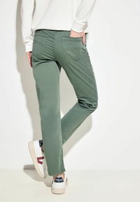 Pantalones verdes de corte slim, con dos bolsillos traseros. Combinados con zapatillas blancas que tienen detalles en rojo y azul marino.