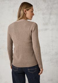 Maglione beige a costine con maniche lunghe e scollatura rotonda, abbinato a jeans in denim blu scuro. Texture morbida con un design aderente.