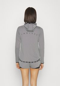 Leichte Kapuzenjacke im schwarz-weißen Netzmuster mit dem Wort "ENDLESS" auf dem Rücken und einem kontrastierenden Taillengummi.