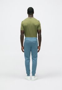 Olívazöld rövid ujjú ing, világoskék mandzsettás szárú melegítőnadrág hátsó zsebbel, fehér tornacipővel párosítva.