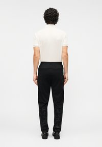 Μαύρο παντελόνι με υφή και διακοσμητικό σχέδιο στο κάτω μέρος του ποδιού, συνδυασμένο με κρεμ κοντομάνικο πουκάμισο. Οπίσθια όψη, με απαλό ύφασμα και ελαστική μέση.