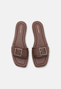 Sandalias deslizantes marrones con una correa ancha y una hebilla cuadrada de plata. Fabricadas con material suave, cuentan con una plantilla acolchada y un diseño de punta cuadrada.