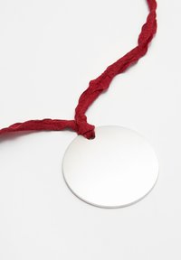 Rund silverhänge på ett knutet rött tygsnöre, med en slät yta och minimalistisk design.