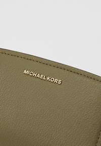 Olive green textured leather product featuring a gold "MICHAEL KORS" logo. The design includes subtle stitching along the edges.