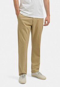 Beige bukser lavet af blødt stof, med sidelommer og en afslappet pasform. Sættet er kombineret med en hvid t-shirt og lyse sneakers.