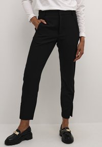 Černé kalhoty na míru se slim fit, s bočními kapsami a malým rozparem na lemu. V kombinaci s černými mokasíny a bílým topem.