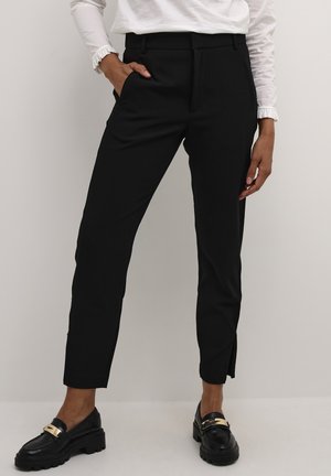 Pantaloni neri su misura con una vestibilità slim, dotati di tasche laterali e una piccola fessura all'orlo. Abbinati a mocassini neri e top bianco.