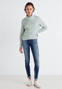 Lys grønn ribbet høyhalset genser, kombinert med smale blå jeans og lys grønne sneakers. Teksturen er myk, med en avslappet passform.