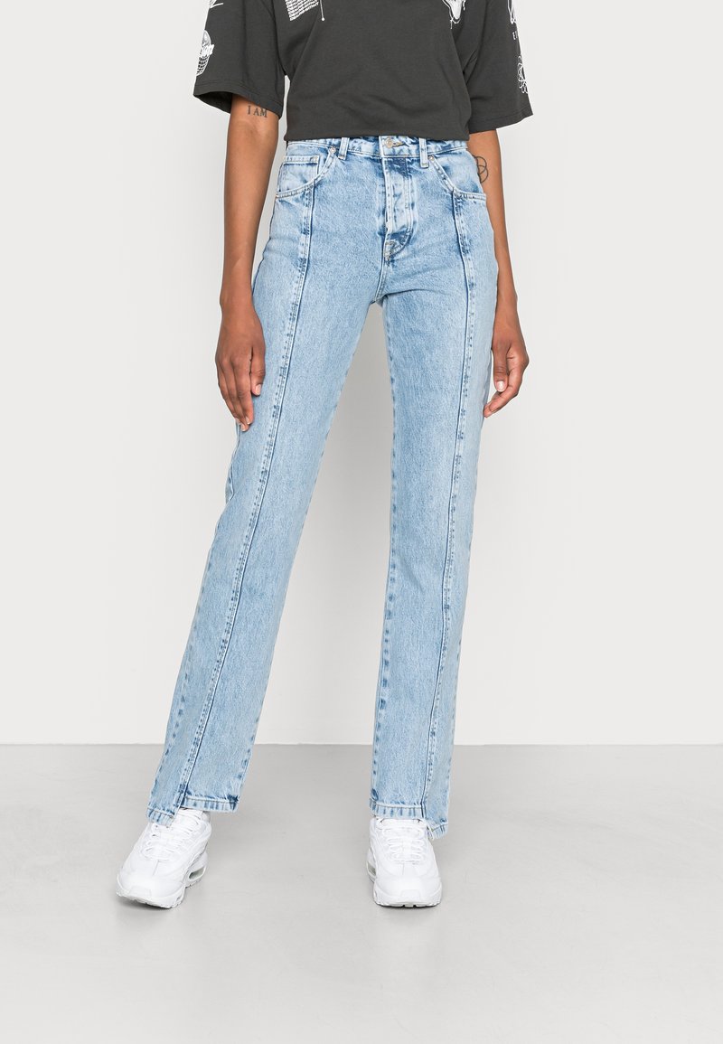 Jeans de cintura alta em azul claro com um design de perna reta, apresentando costura contrastante e uma textura de denim suave, combinados com ténis brancos.