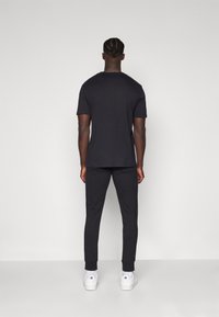 Zwarte katoenen T-shirt en bijpassende joggers, beide fitted, met ribboordmanchetten. Witte sneakers maken de look compleet. Minimalistisch ontwerp, geen patronen.