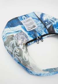 Kék mintás táska, amely virágos minták és absztrakt grafikák keverékét tartalmazza, fekete cipzárral és hozzácsatolt címkével.