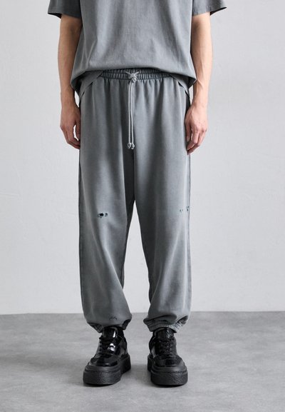 Gray joggers with drawstring waist, loose fit, and distressed details. Paired with black platform sneakers featuring glossy finish.