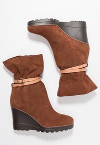 Bruna mockaskor med kilklack, med en slouchig topp, som har ett ljust tan-färgat spänne och en texturerad svart plattformssula.