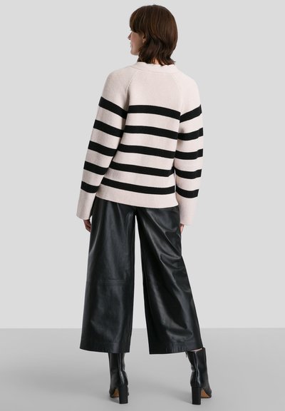 Maglione lavorato a maglia rosa chiaro con righe orizzontali nere, dotato di un colletto alto e un fit rilassato, abbinato a pantaloni in pelle nera a gamba larga.