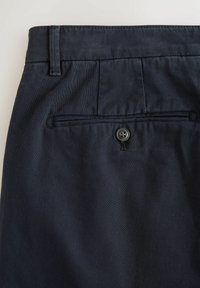Dark navy trousers back pocket with a button closure and a belt loop on a plain light background.