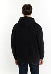 Sort hættetrøje med en afslappet pasform, ribbede manchetter og talje. Blød tekstur, minimalistisk design. Set fra ryggen.