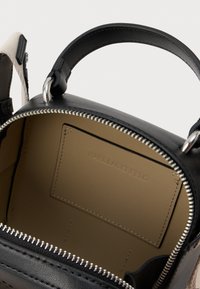 Svart lærveske med sølvglidelås åpnet for å vise en beige innvendig lomme preget med "Karl Lagerfeld" og svart håndtak på hvit bakgrunn.