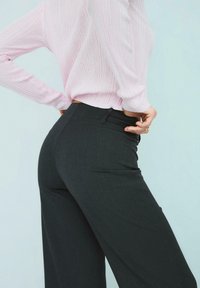 Crne krojene hlače širokih nogavica s glatkom teksturom i dva prednja džepa. Uparene s dugim ručnim topom u svijetlo ružičastoj boji s rebrastim uzorkom.