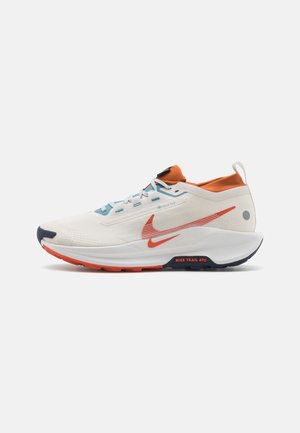 Chaussure de course Nike blanche et orange avec des accents bleus, un logo Swoosh rouge et le texte "Nike Trail ATC" sur la semelle, vue de côté.