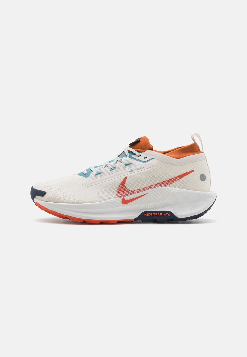 Chaussure de course Nike blanche et orange avec des accents bleus, un logo Swoosh rouge et le texte "Nike Trail ATC" sur la semelle, vue de côté.